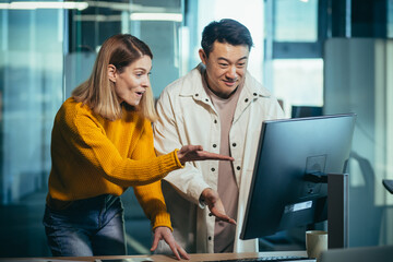 Employees of the IT company look at the computer monitor in surprise, an Asian man and a woman work in a modern office