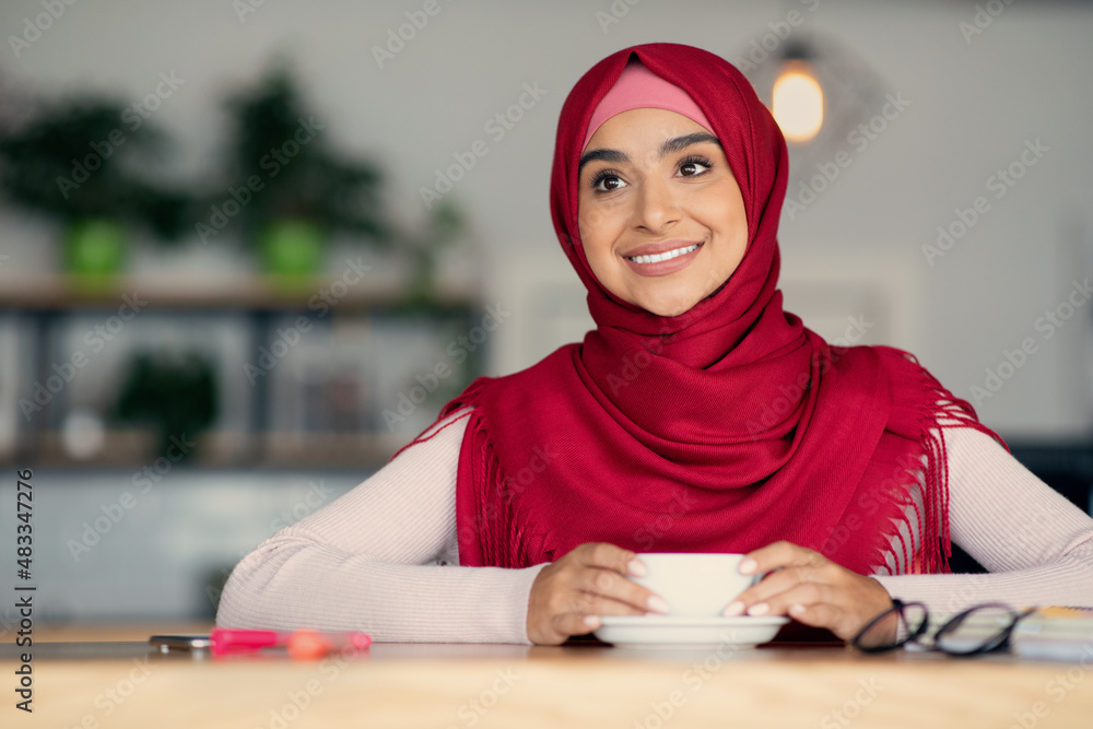 Wall mural Relaxed middle eastern woman in hijab enjoying coffee at cafe