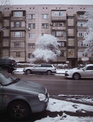 a street with cars passing by. a post-soviet panel house in winter