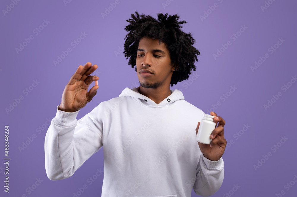 Wall mural african american teenager holding jar and pill over violet studio background. health care, treatment