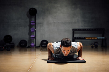 Sport caucasian man goes down for push-ups in a dark gym.