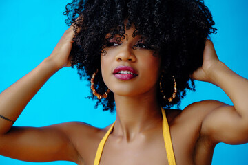 young beautiful woman with hands on curly afro hairstyle posing in studio looking to the side