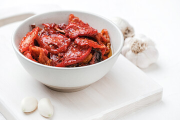 Sun dried tomatoes  on white bowl, white wooden background. Dried tomatoes with olive oil, salt, herbs and garlic recipe.  Top view,  copyspace.