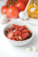 Sun dried tomatoes  on white bowl, white wooden background. Dried tomatoes with olive oil, salt, herbs and garlic recipe.  Top view,  copyspace.