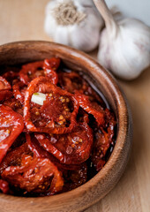 Sun dried tomatoes  in wooden bowl. Dried tomatoes with olive oil, rosemary, salt, herbs and garlic recipe.  Dark background. 