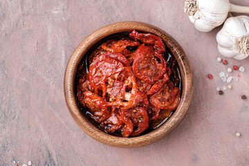 Sun dried tomatoes  in wooden bowl. Dried tomatoes with olive oil, rosemary, salt, herbs and garlic recipe.  Dark background. 