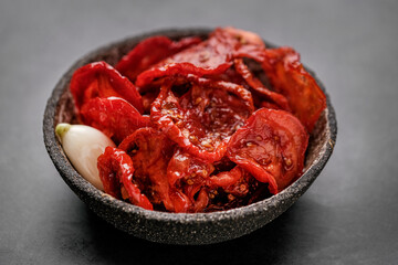 Sun dried tomatoes  in wooden bowl. Dried tomatoes with olive oil, rosemary, salt, herbs and garlic recipe.  Dark background. 