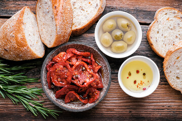Italian ingredients  food background. Slices of ciabatta bread  on wooden board with olives, dried tomatoes, oil, rosemary and herbs on rustic wooden background. top view.