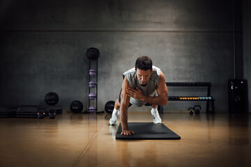 Fototapeta na wymiar Strong caucasian man looks down while does push-ups with one hand in a dark gym.