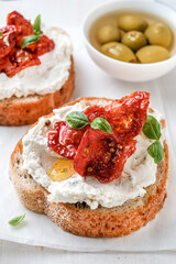 Two bruschettas with ricotta cheese, olive and dried tomatoes on ciabatta bread on white background. Olive oil and spices decorated. Copyspace.