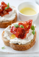 Two bruschettas with ricotta cheese, olive and dried tomatoes on ciabatta bread on white background. Olive oil and spices decorated. Copyspace.