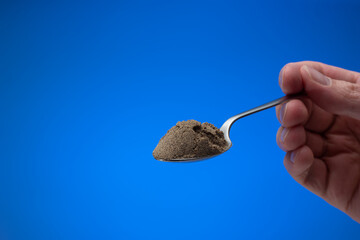 Finely ground black pepper powder in a small silver spoon. Close up studio shot, isolated on blue background