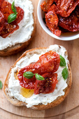Two bruschettas with ricotta cheese, olive and dried tomatoes on ciabatta bread on white background. Olive oil and spices decorated. Copyspace.