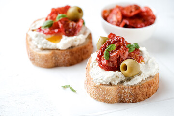 Two bruschettas with ricotta cheese, olive and dried tomatoes on ciabatta bread on white...