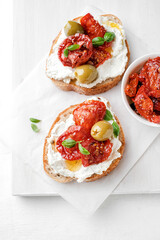 Two bruschettas with ricotta cheese, olive and dried tomatoes on ciabatta bread on white...