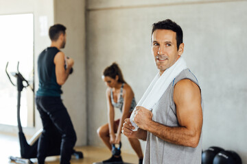Fototapeta na wymiar Smiling attractive sporty fit man stands and poses in a gym looking one side.