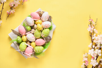 Easter pastel coloful eggs and spring blooming flowers on yellow background with copy space. View from above. Easter greeting card.