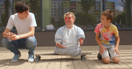 CZ, Kladno, Armenska, 4.8.2021 The boys sit down at the woman's level. Simplification of communication. Portrait of happy woman with friends. Skate on the ground. - obrazy, fototapety, plakaty