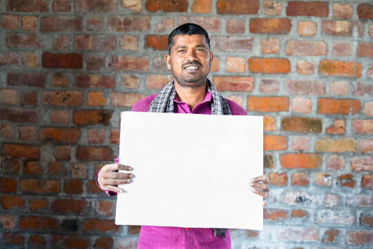 Smiling Construction Worker Holding Empty Sign Board At Site By Looking At Camera - Concept Of Advertisement For Welfare Schemes