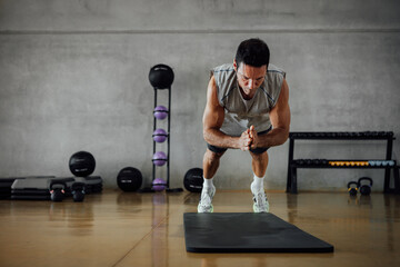 Strong fitness man jumps while does push-ups in gym.