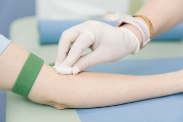 Taking a blood test from a vein in the treatment room. Nurse pricking a syringe with a needle into the patient hand. Swab pressed against the injection site during blood donation. Tube with blood.