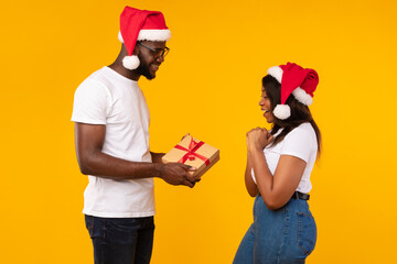 Black Boyfriend Giving Christmas Gift To Girlfriend Over Yellow Background