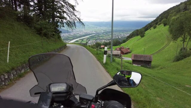 POV Biker rides a motorcycle on scenic mountain road in Liechtenstein. Steering wheel view. Motorcyclist on Motorbike goes by narrow alpine road among the mountain forest and cliffs. First-person view