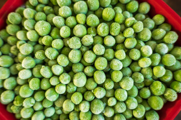 frozen frosty green peas in red ceramic bowl closeup