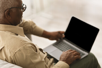 Unrecognizable Senior African Man Using Laptop With Blank Screen Indoors