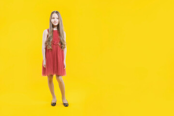 A cute teenage girl with long blond hair is standing on a yellow background smiling. Full-length student. Copy space.