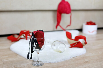 Wine glass with female thong panties, removed red bra and shoes on a floor near sofa. Romantic...