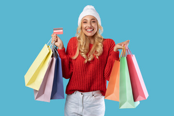 Cheerful woman holding credit card carrying shopping bags in winter