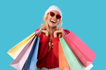 Excited blonde woman holding shopping bags at studio