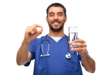 healthcare, profession and medicine concept - happy smiling doctor or male nurse in blue uniform with pill and glass of water over white background
