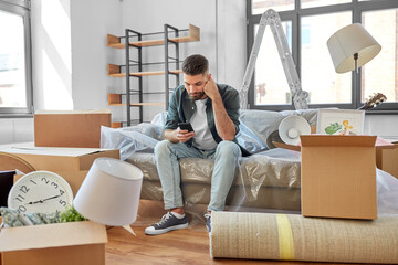 moving, eviction and real estate concept - sad man with smartphone and boxes at new home