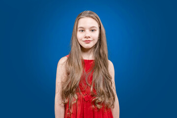 Fototapeta premium Pupil. A cute teenage girl with long blond hair is standing on a blue background smiling