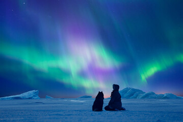 Woman with her dog admiring Northern Lights. Aurora Borealis over arctic winter landscape.