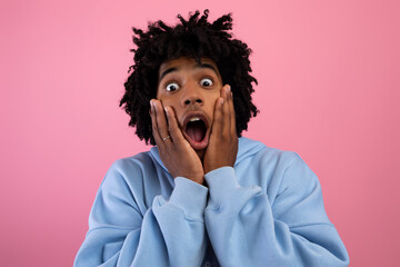 Cool black teen guy touching his face, screaming in terror on pink studio background