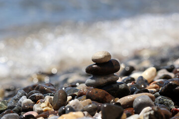 Fototapeta na wymiar Tower of pebble stones on blurred background of the sea waves. Beach vacation, balance and relax concept