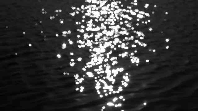 Black water texture with white sun or moon light bokeh reflection. Dark surface organic 4k video background. Rippling and sparkling river or lake