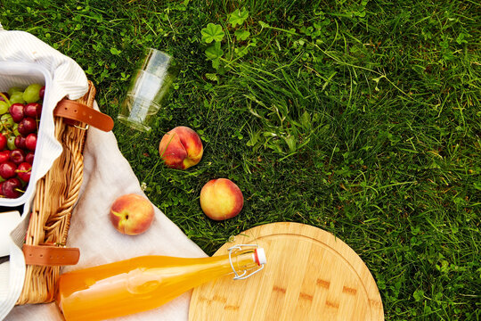 leisure and drinks concept - close up of food, drinks and basket on picnic blanket on grass