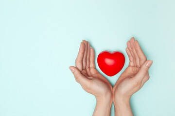 Health, medicine and charity concept - close up of female hands with small red heart.