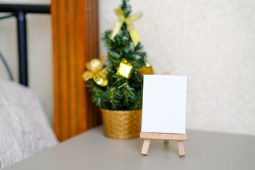 Small decorative wooden easel with white blank canvas against the background of a Christmas tree. New life from scratch. Start over again.