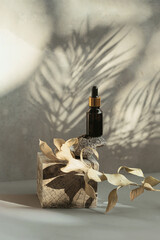 Amber glass bottle of essential oil or serum with pipette on wooden podium with grey concrete wall...