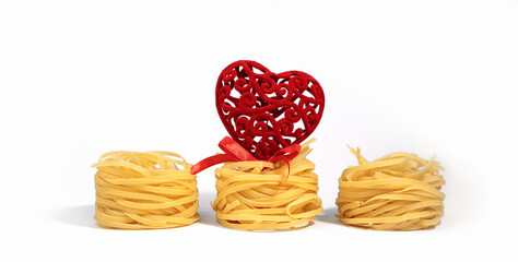 Food for Valentine's Day. Italian pasta. Spaghetti Capellini, with a creative red heart with a bow, isolated on a white background, with hard shadows. Pasta in the form of nests on Valentine's Day. 