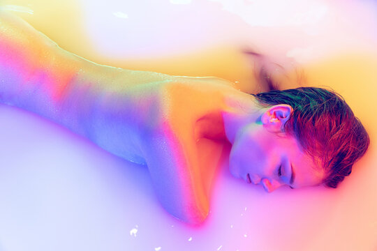 Closeup female hips, bottocks in the milk bath with soft pink neon glow. Beauty, fashion, style, bodycare, spa concept.