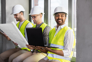 architecture, construction business and people concept - group of male architects in helmets with laptop, blueprint and clipboard working at office