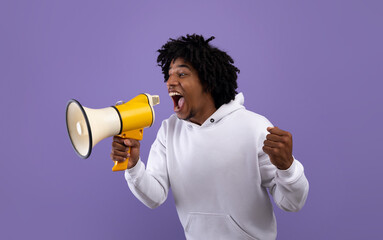 Emotional black adolescent shouting into megaphone, making announcement over violet studio...