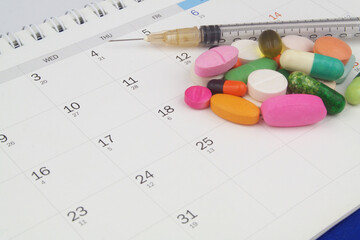 Colorful drugs and pills, syringe on calendar background.	