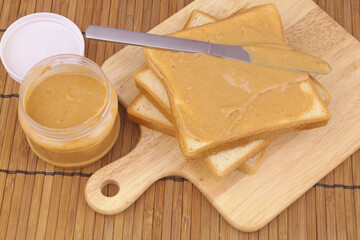 Peanut butter with bread slices spread on cutting board	